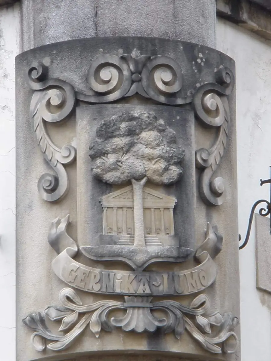 Escudo con un árbol sobre un edificio con columnas y la leyenda «Gernika-Lumo» en el ayuntamiento de Gernika.