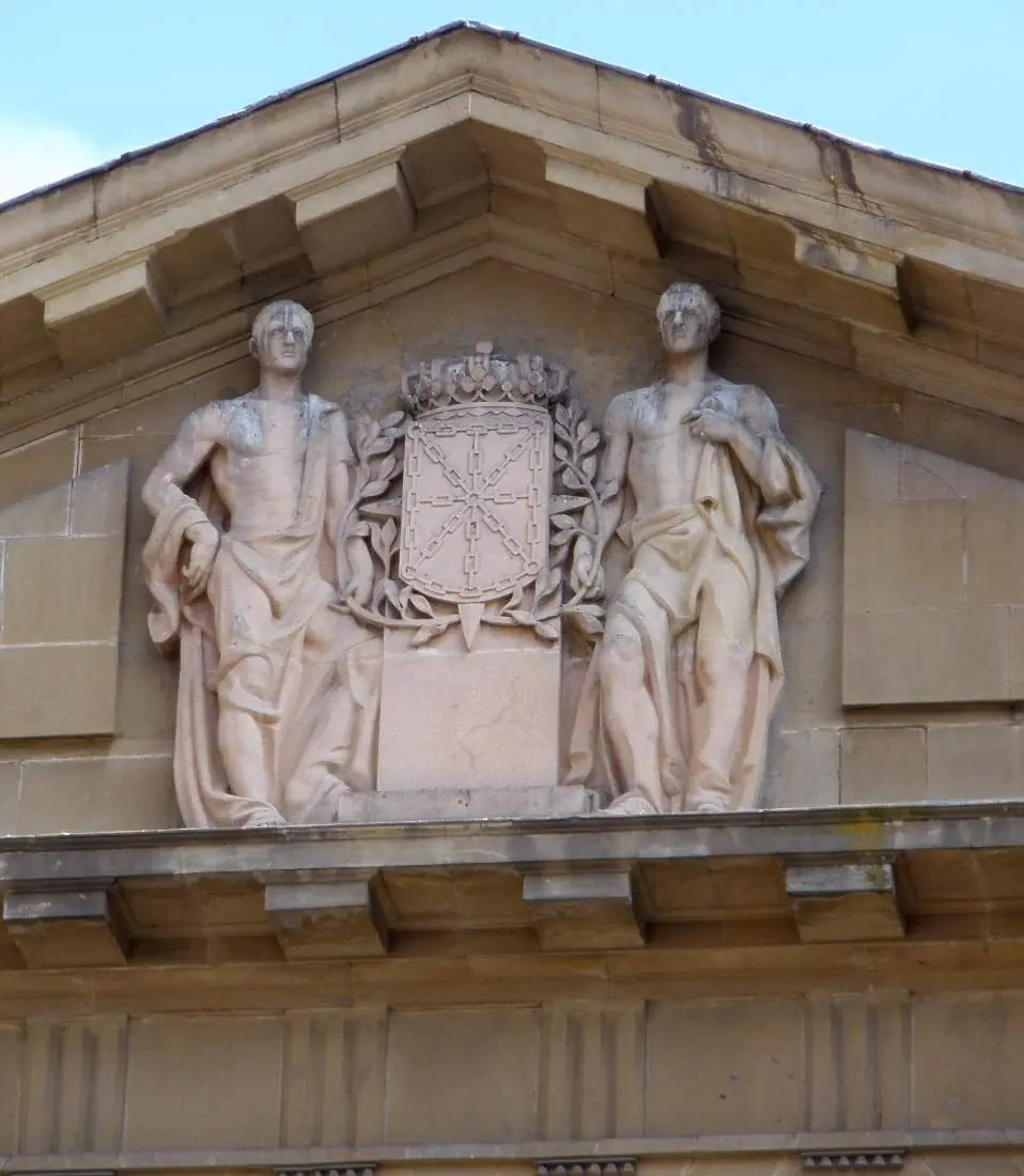 Armas de Navarra con corona entre dos figuras alegóricas en el frontón del Palacio de Navarra, Pamplona.