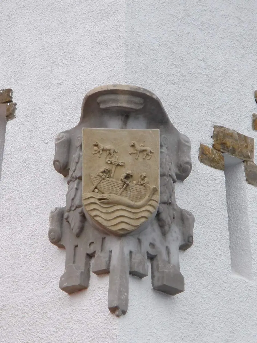 Escudo con una embarcación con dos tripulantes, ondas y dos animales sobre ella en Bermeo.