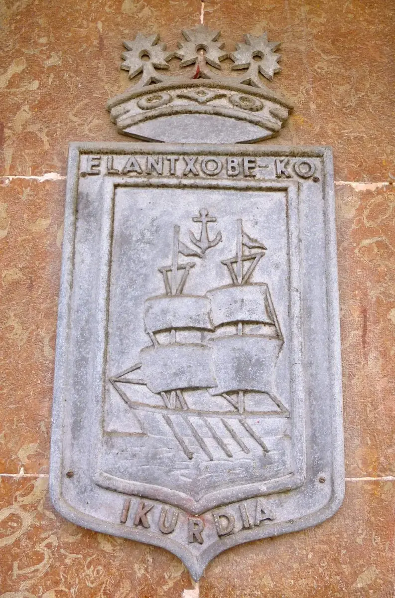 Escudo con un barco de velas y un ancla bajo una corona, con las inscripciones «Elantxobe ko» e «Ikurdia», en Elantxobe.