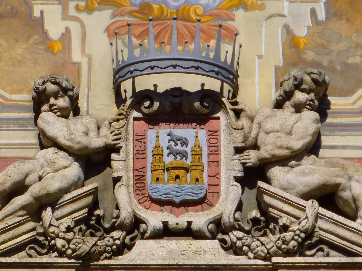 Escudo policromado bajo corona con una torre, dos lobos y un río, y la leyenda «Corona real, noble y leal», en el ayuntamiento de Durango.