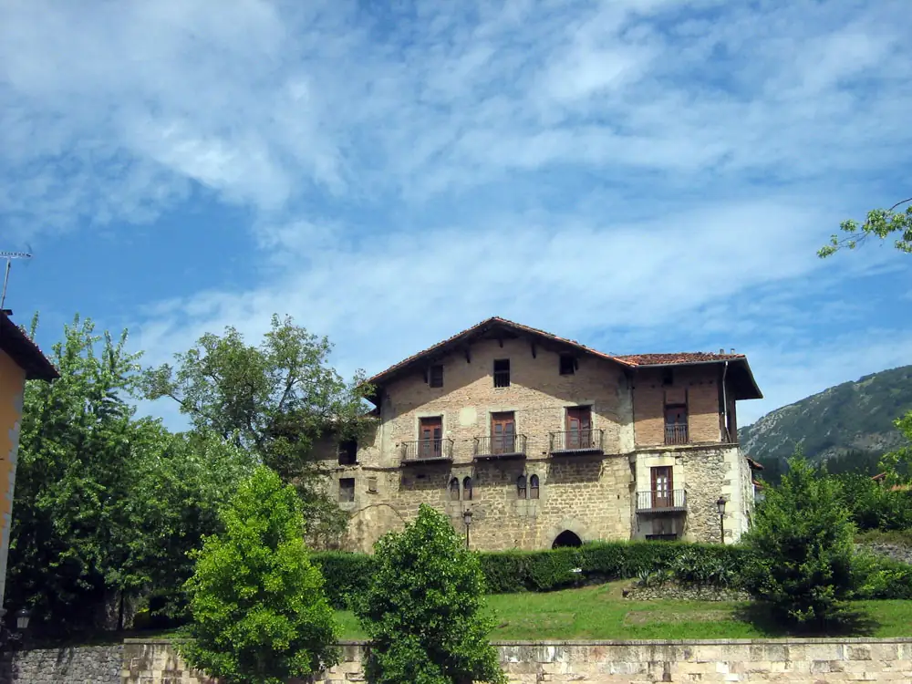 La casa-torre de Balda, con fachada de piedra y balcones de madera, sobre una pradera.