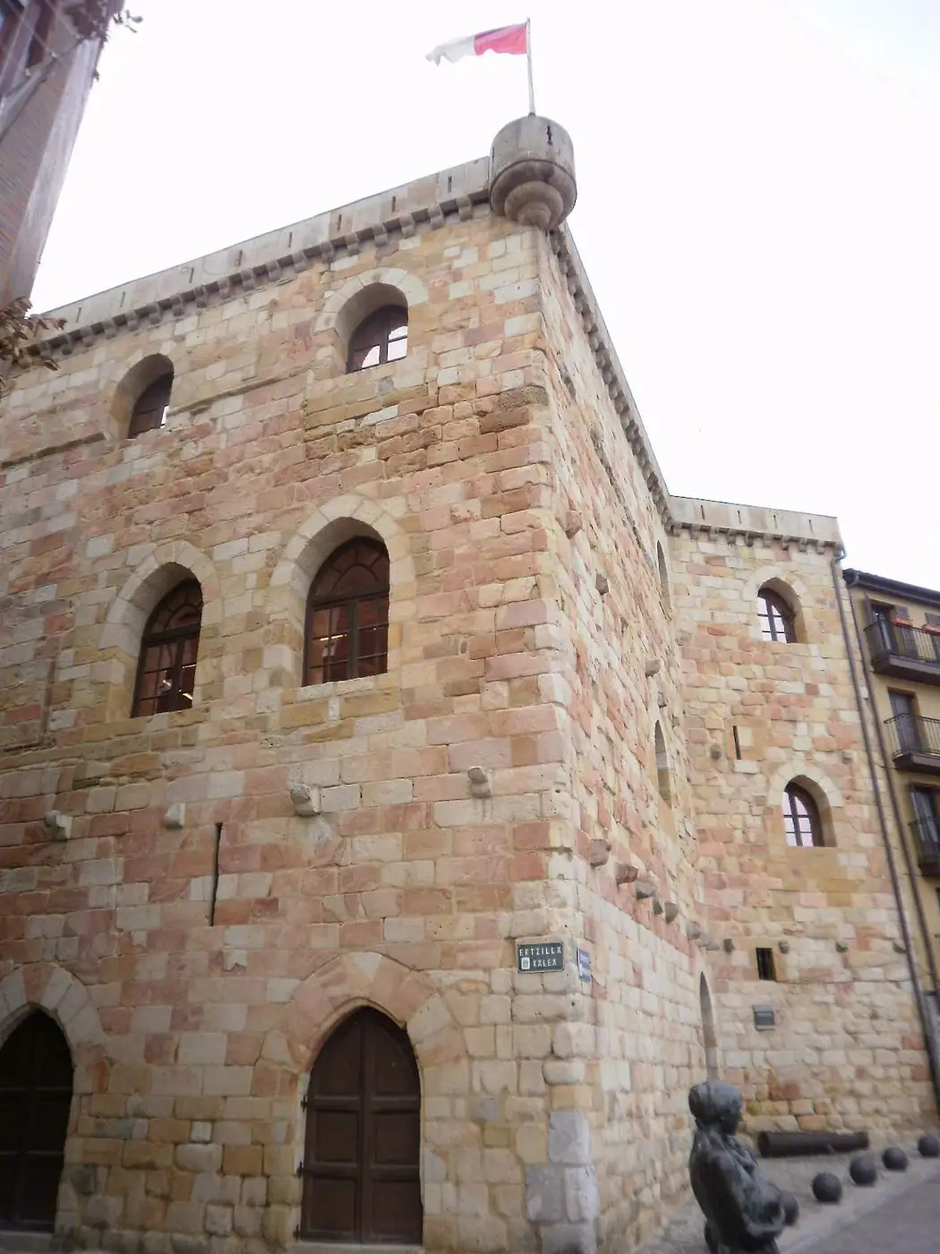 La torre de Ercilla, de sillería, con ventanas de arco y un remate cilíndrico en la esquina, y una escultura en primer plano.