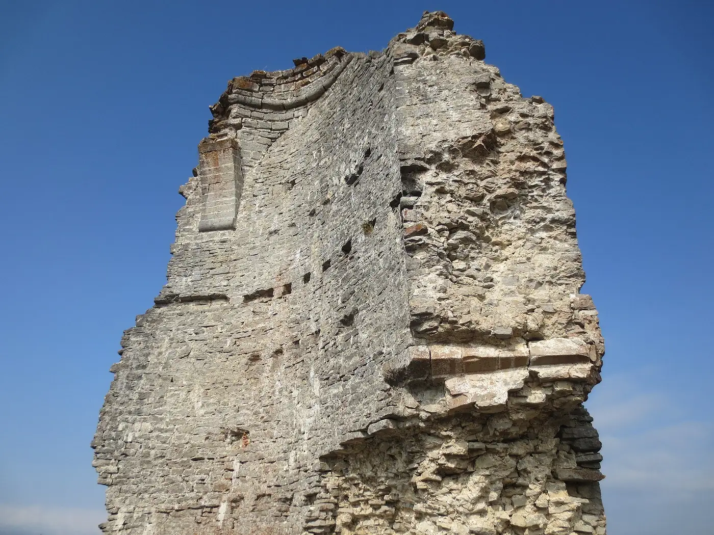 Muro en ruina del castillo de Guevara, con hileras de agujeros en la fábrica y restos de una moldura curva en lo alto.