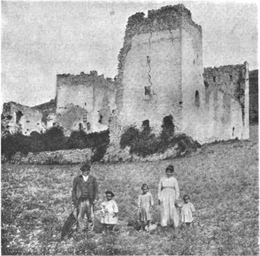 Ruinas del palacio de Guevara, con una torre de planta rectangular y unas personas posando delante, en una fotografía de la Geografía General del País Vasco-Navarro.