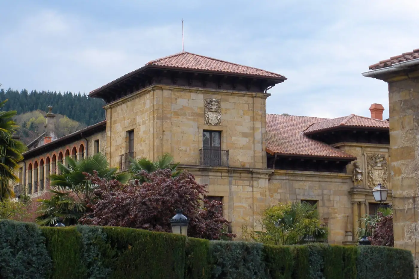Cuerpo con tejado de cuatro aguas y galería de arcos del palacio de Lazkao, entre palmeras.