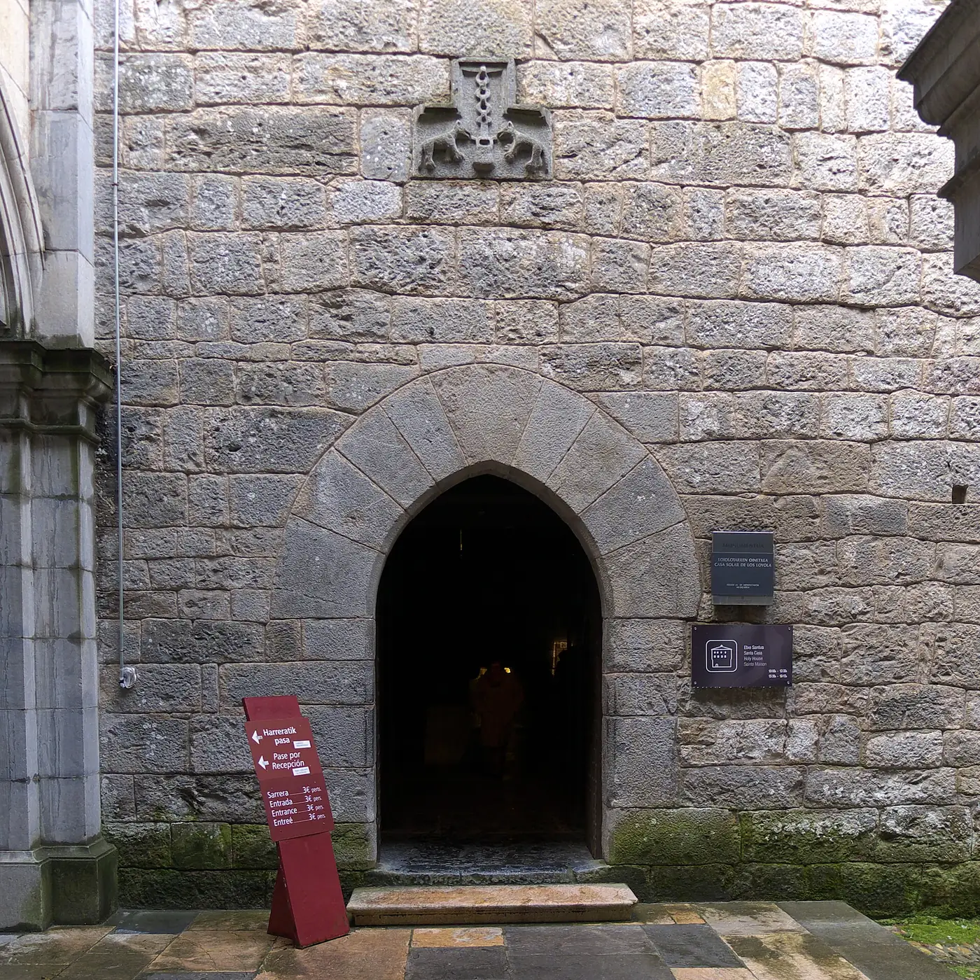 Portal de arco apuntado en el muro de sillería de la casa torre de los Oñaz y Loiola, con un escudo sobre la puerta.