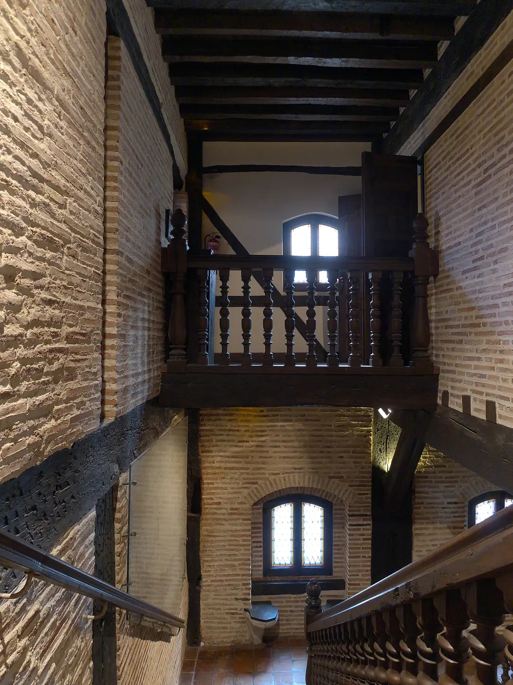 Escalera y galería de madera en el interior de la Santa Casa de Loiola, entre muros de ladrillo.