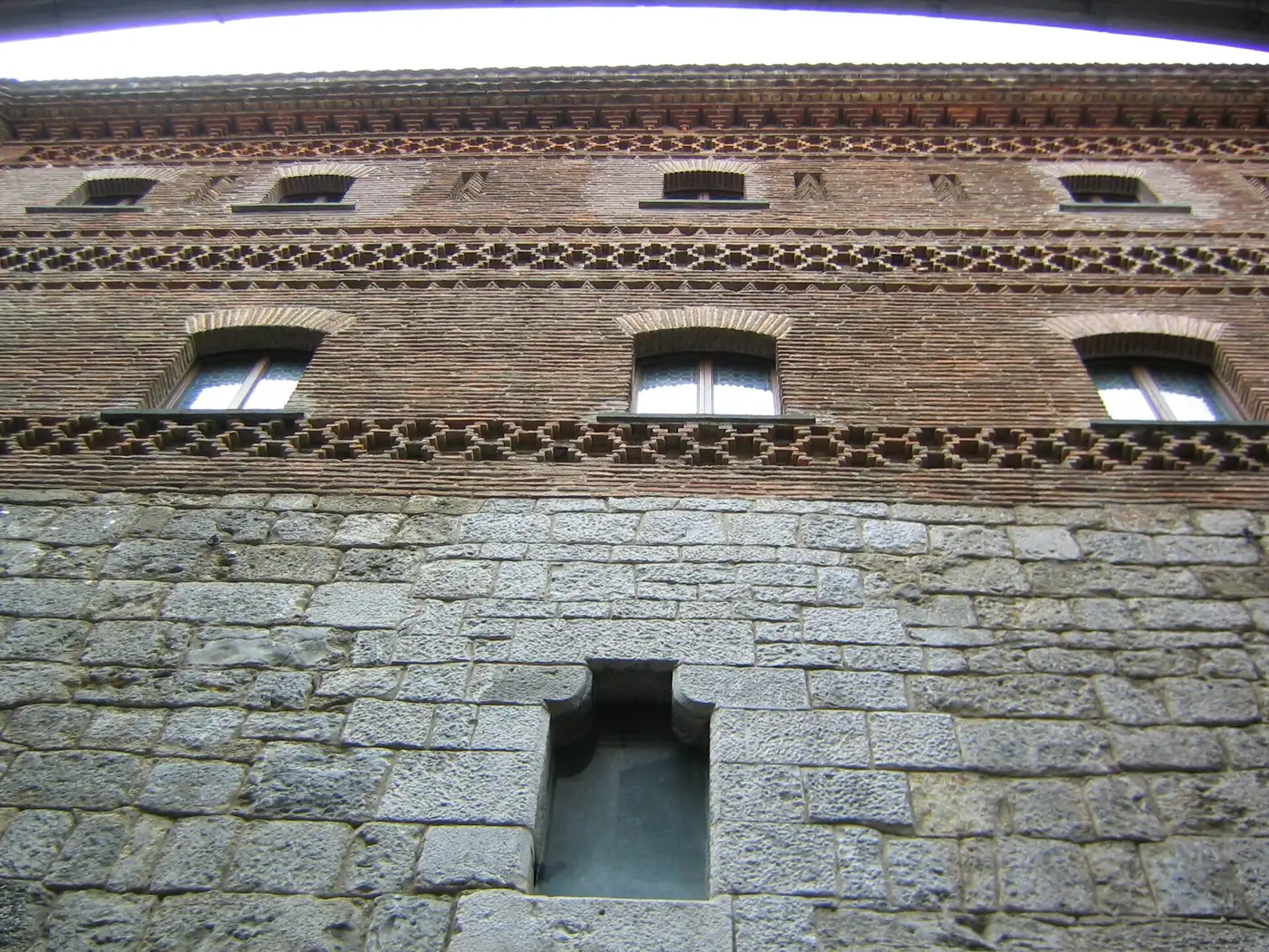 Detalle de la fachada de ladrillo de la Santa Casa de Loiola, con frisos decorativos y un hueco estrecho en el zócalo de sillería.