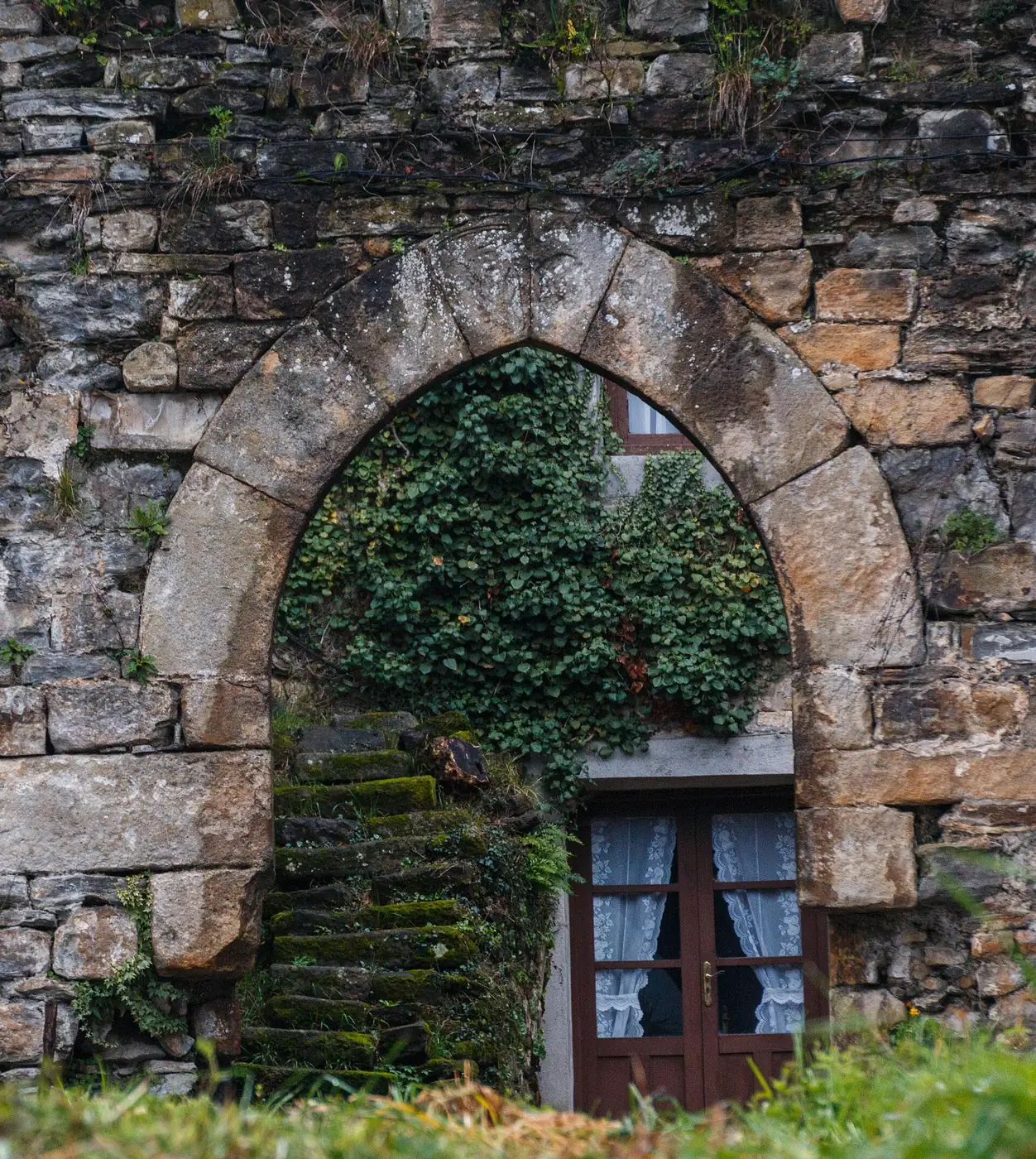 Arco apuntado de piedra con hiedra en un muro de la torre de Muxika.