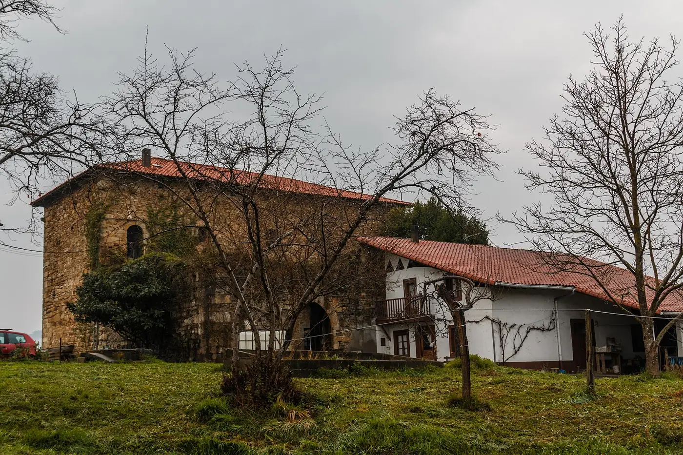La torre de Muxika sobre una pradera, con un anexo de tejado a dos aguas a su derecha.