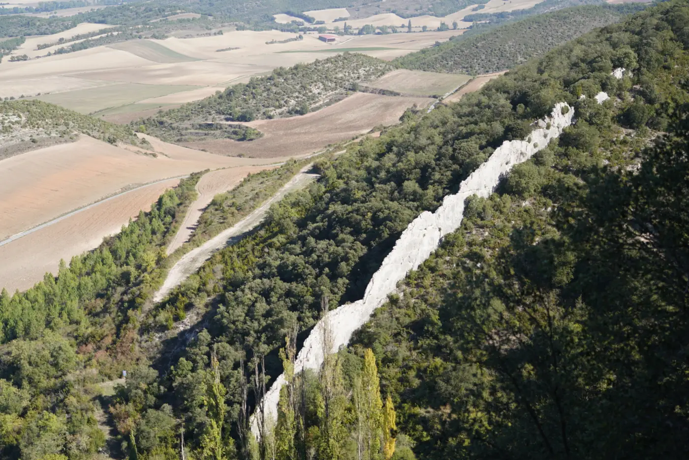 Línea blanca de muralla que baja por la ladera del castillo de Portilla, con campos de cultivo al fondo.